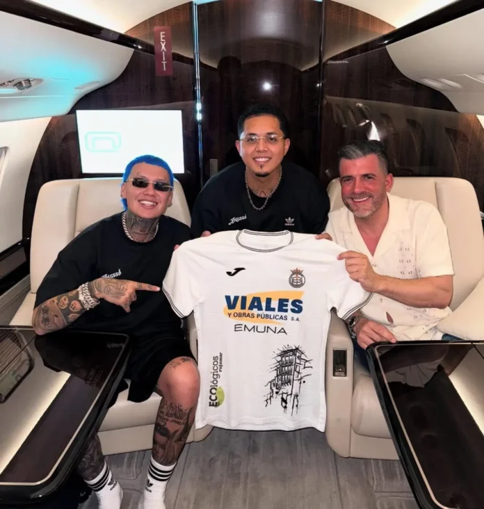 “Blessd y ejecutivos del club Conquense durante la firma de la alianza, con camiseta blanca y negra del equipo, en estadio La Fuensanta.”